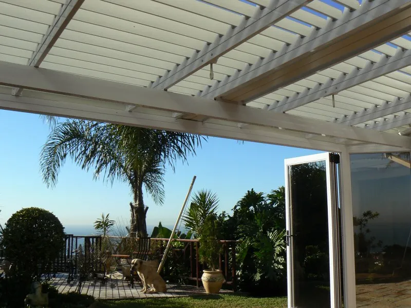 White adjustable louvres over a deck with folding glass doors, palms and a flat sea horizon beyond