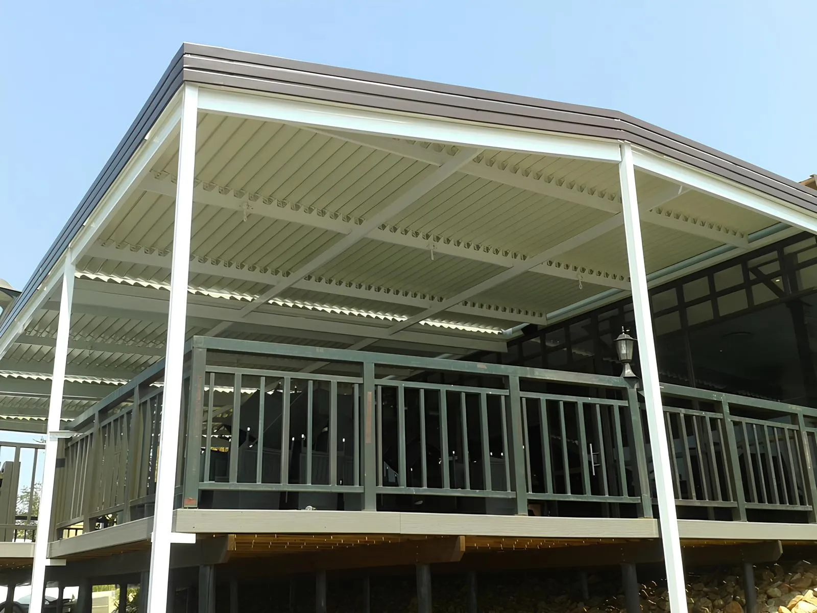 White adjustable louvres over a raised deck with a dark balustrade, dry grass slope behind