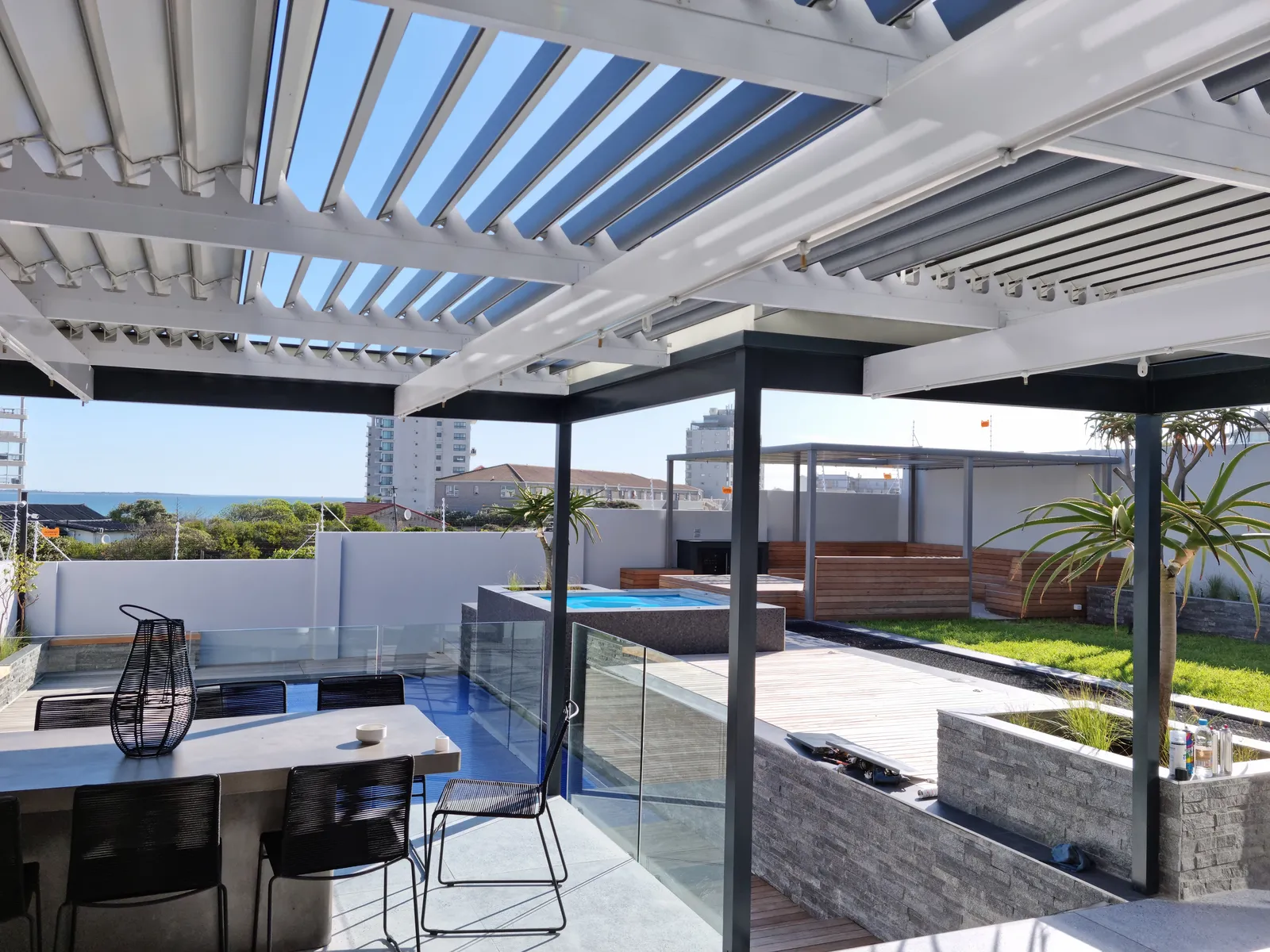 White adjustable louvre awnings over a rooftop terrace with a sea view, fitted by AL Patio Solutions