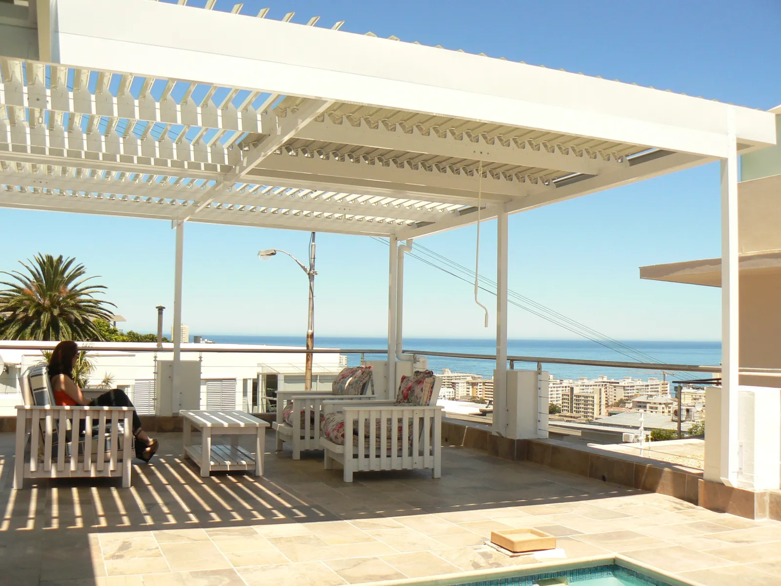 White adjustable louvre awning over a Sea Point terrace with palm trees and the Atlantic behind